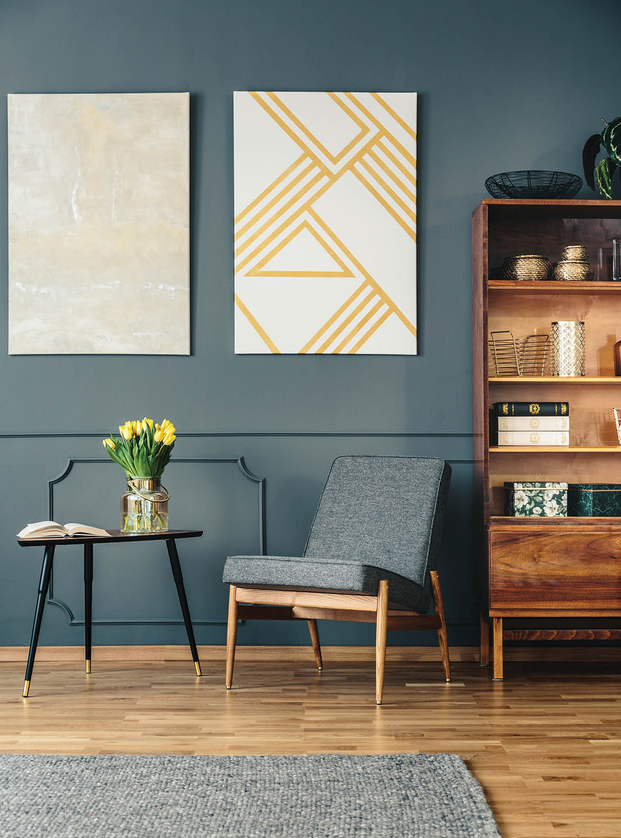 Gray, upholstered chair next to an elegant, wooden bookcase in a reading corner of a dark living room interior with molding