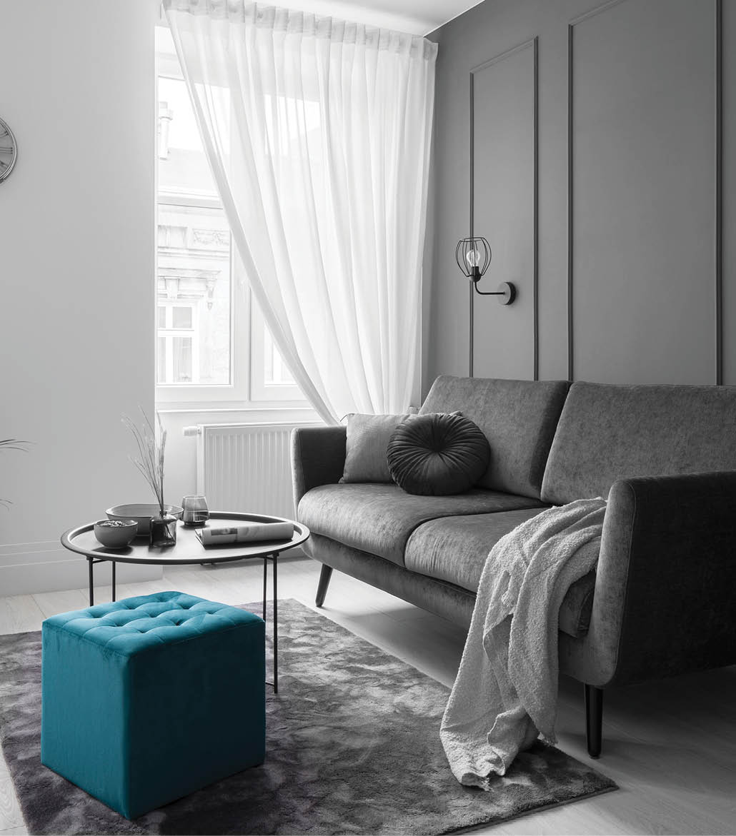 Small living room with teal blue wall with decorative molding, modern sofa, black coffee table and square, quilted ottoman