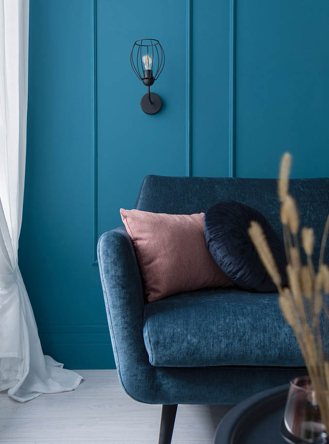 Close-up on charming blue sofa with decorative pillows in living room with teal blue wall with molding