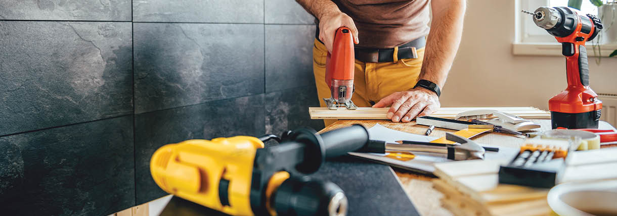 Man cutting piece of wood on the table with electric Jigsaw at home