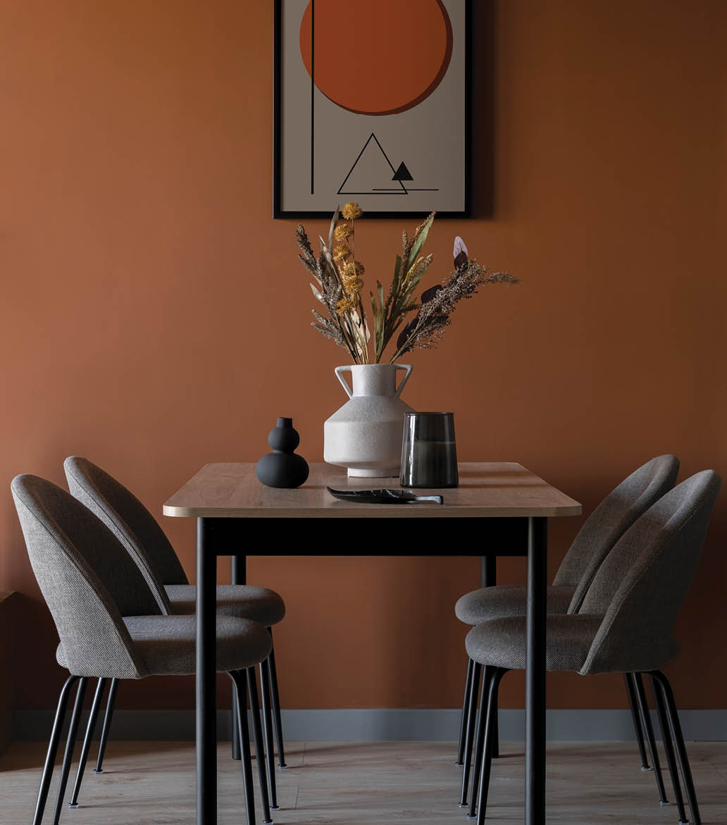 Eclectic dining room with art on modern rusty colored wall, simple table with four elegant chairs