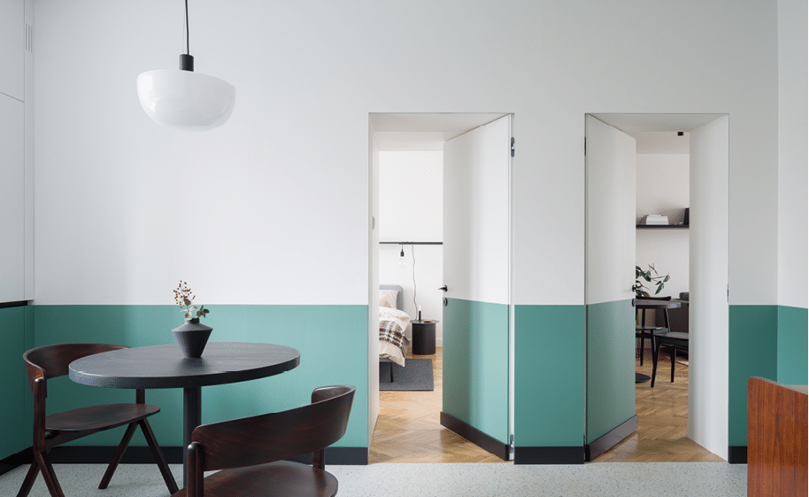 Modern room with dark, dining table with two chairs, half white and green walls and open doors to bedroom and living room