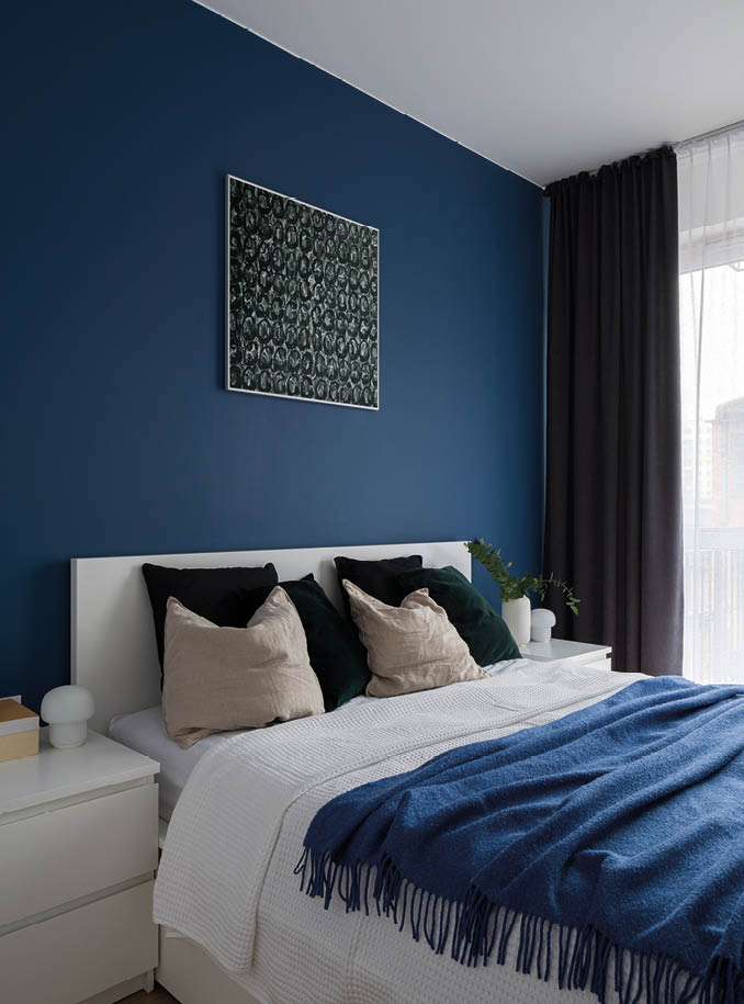 Navy blue color on wall behind comfortable bed in modern bedroom with white furniture