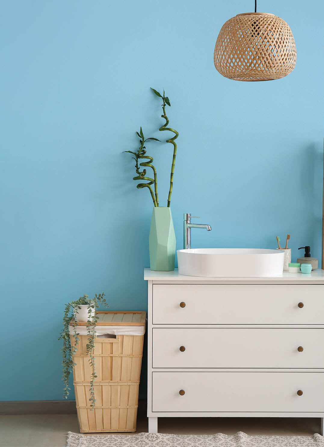 Sink, bath accessories and vase with bamboo stems on drawers near blue wall