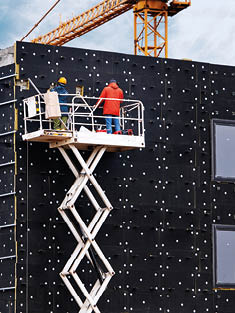 Professional construction workers on scissors mechanism elevator insulating wall facade with mineral wool for thermal protection. Industrial climbers wearing safety harness insulated wall facade