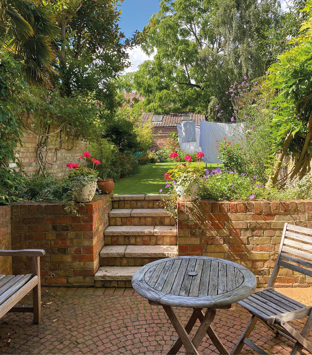 View from a back patio in summertime, looking over a garden with flowers and a stone wall.