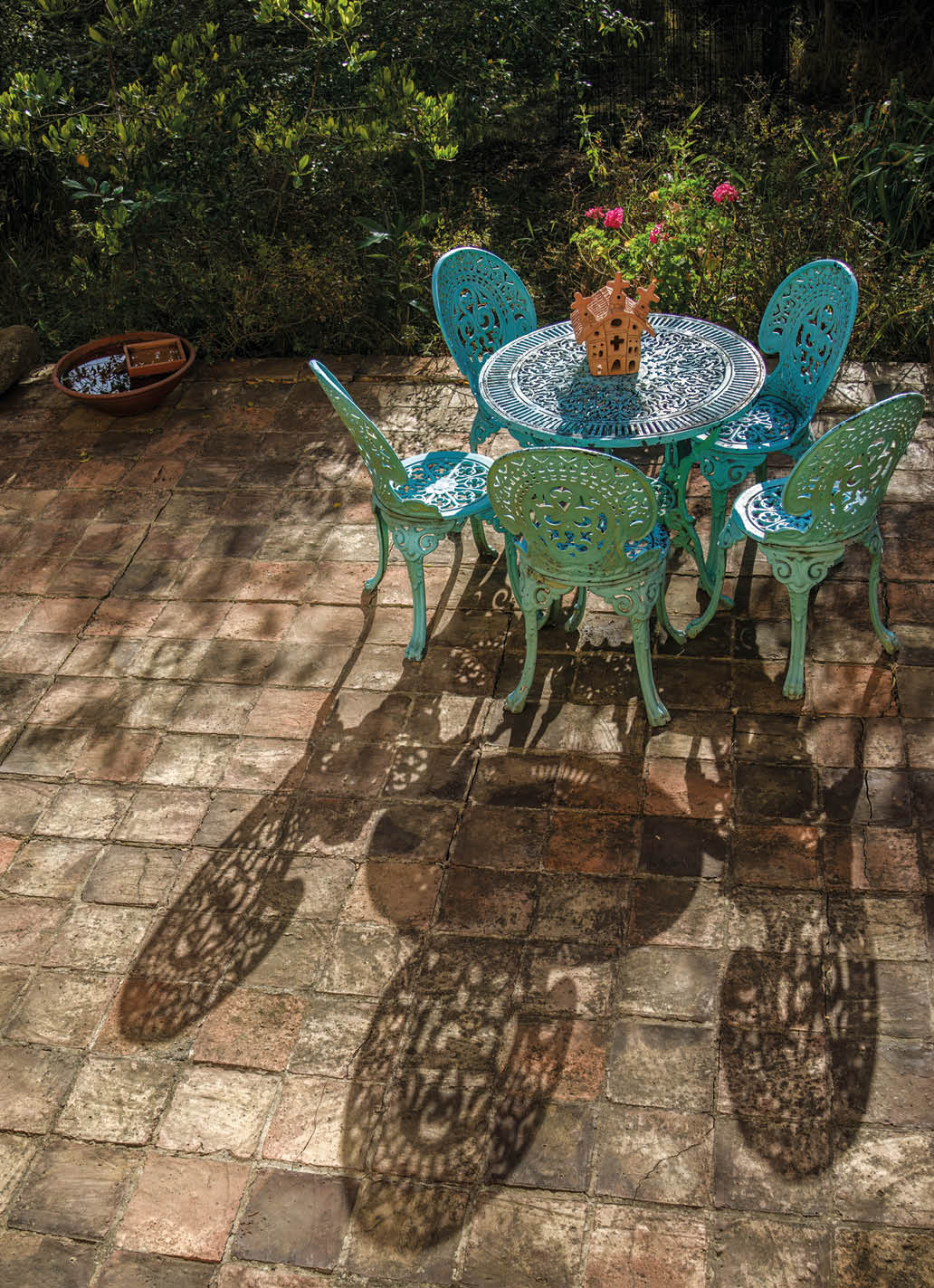 A metallic garden furniture casting shadows on a clay tile terrace, at sunset, in a garden at the eastern Andean mountains of central Colombia.