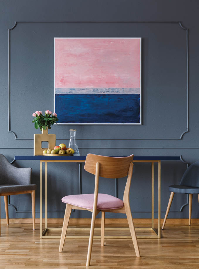 Pink wooden chair at table in dining room interior with painting on grey wall with molding