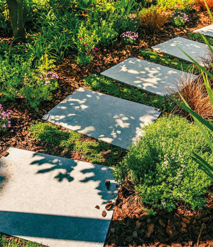 Detail of garden path with stone slabs with bark mulch and native plants. Landscaping and gardening concept.