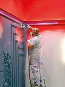Construction worker spray painting interior wall using airless paint sprayer