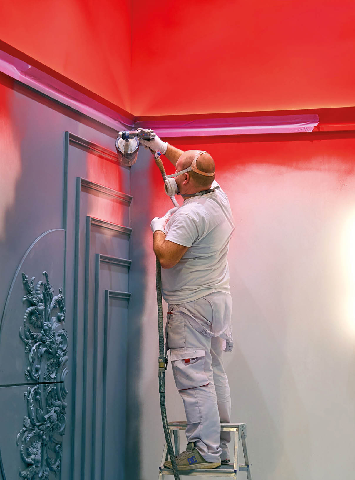 Construction worker spray painting interior wall using airless paint sprayer