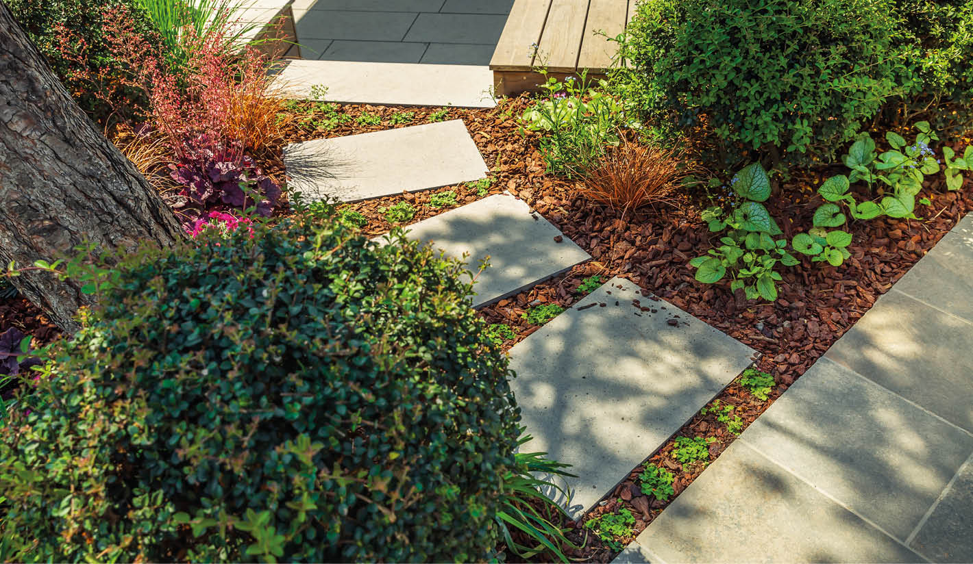 Detail of garden path with stone slabs with bark mulch and native plants. Landscaping and gardening concept.