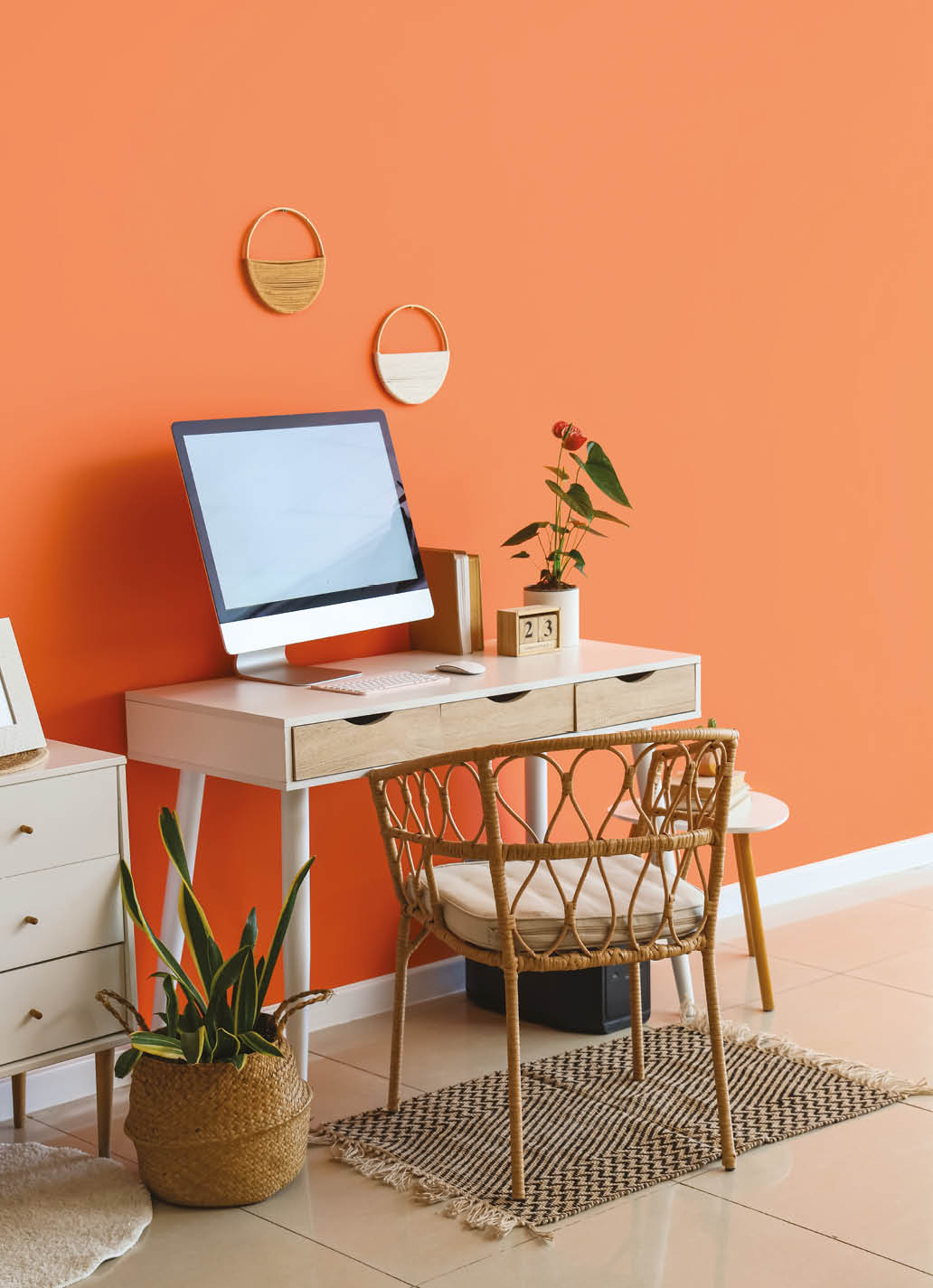 Comfortable workspace with modern computer, anthurium flower and calendar near orange wall