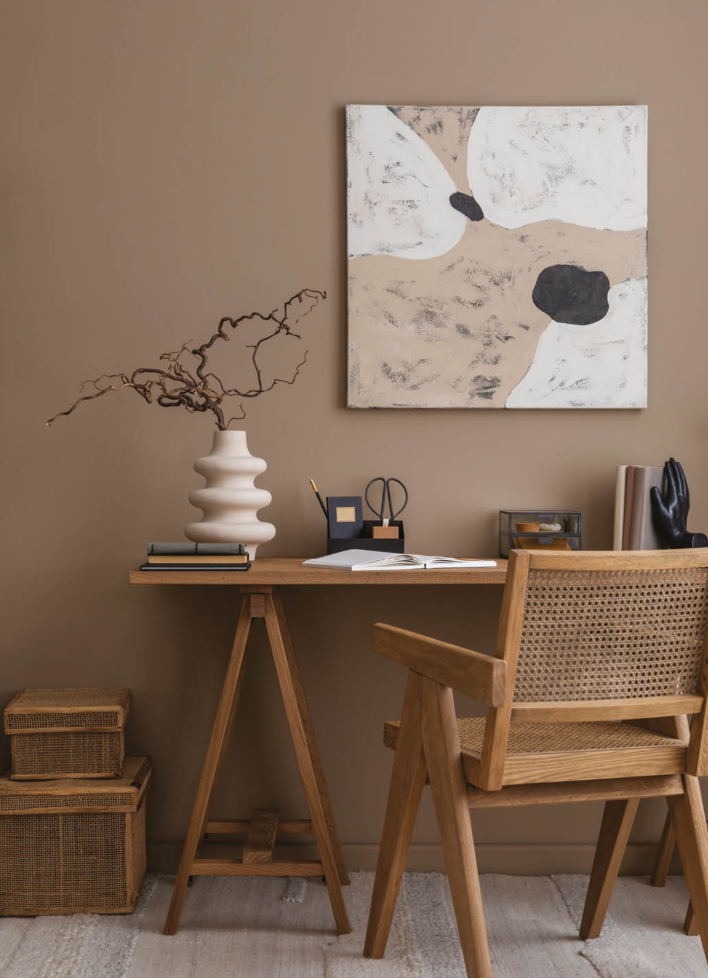 Aesthetic composition of workspace interior with mock up poster frame, wooden desk, rattan chair, stylish lamp, vase with dried flowers, book and personal accessories. Home decor. Template.