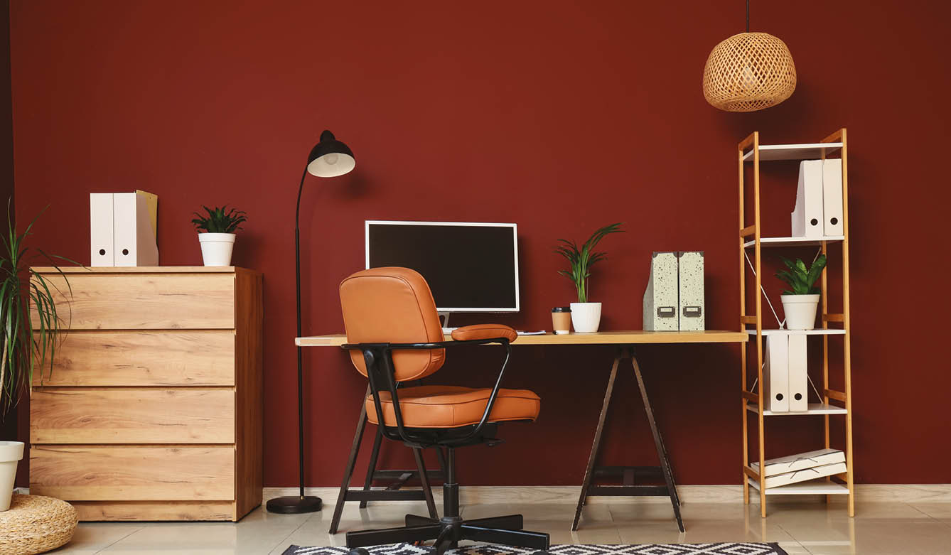 Modern home office interior with computer monitor, brown leather chair, wooden desk, and red wall decor